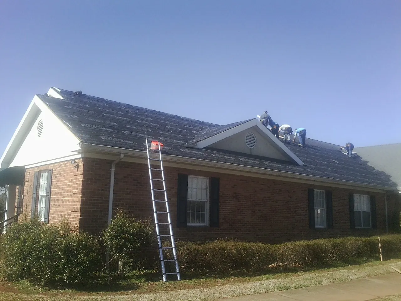 Crew tearing shingles off a brick ranch roof with a ladder set — Emergency Roof Repair work by our crew in Ranchita