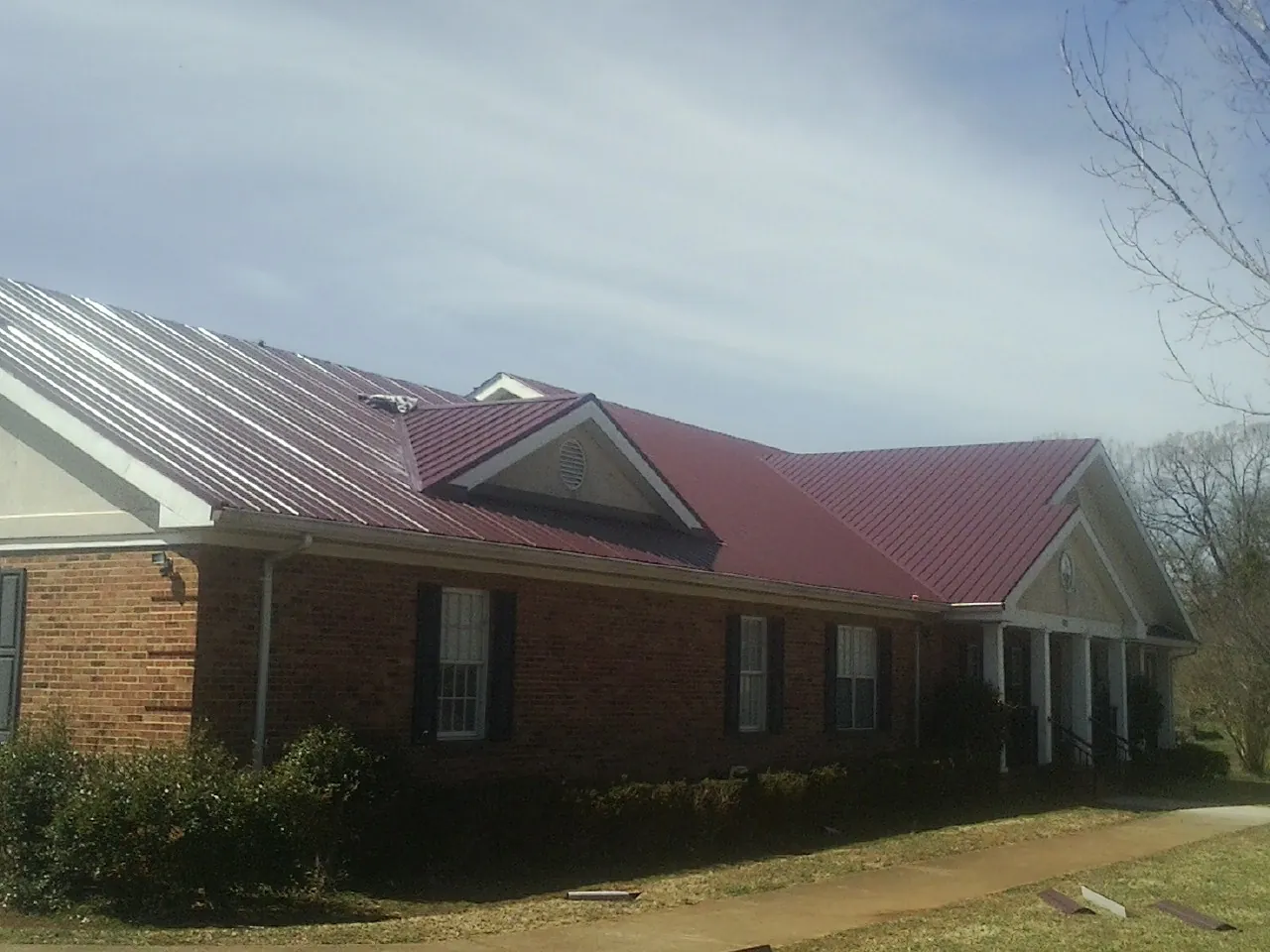 Red metal roof with gabled entries on a long brick building, from a Hail Damage Roof Repair job in Ranchita