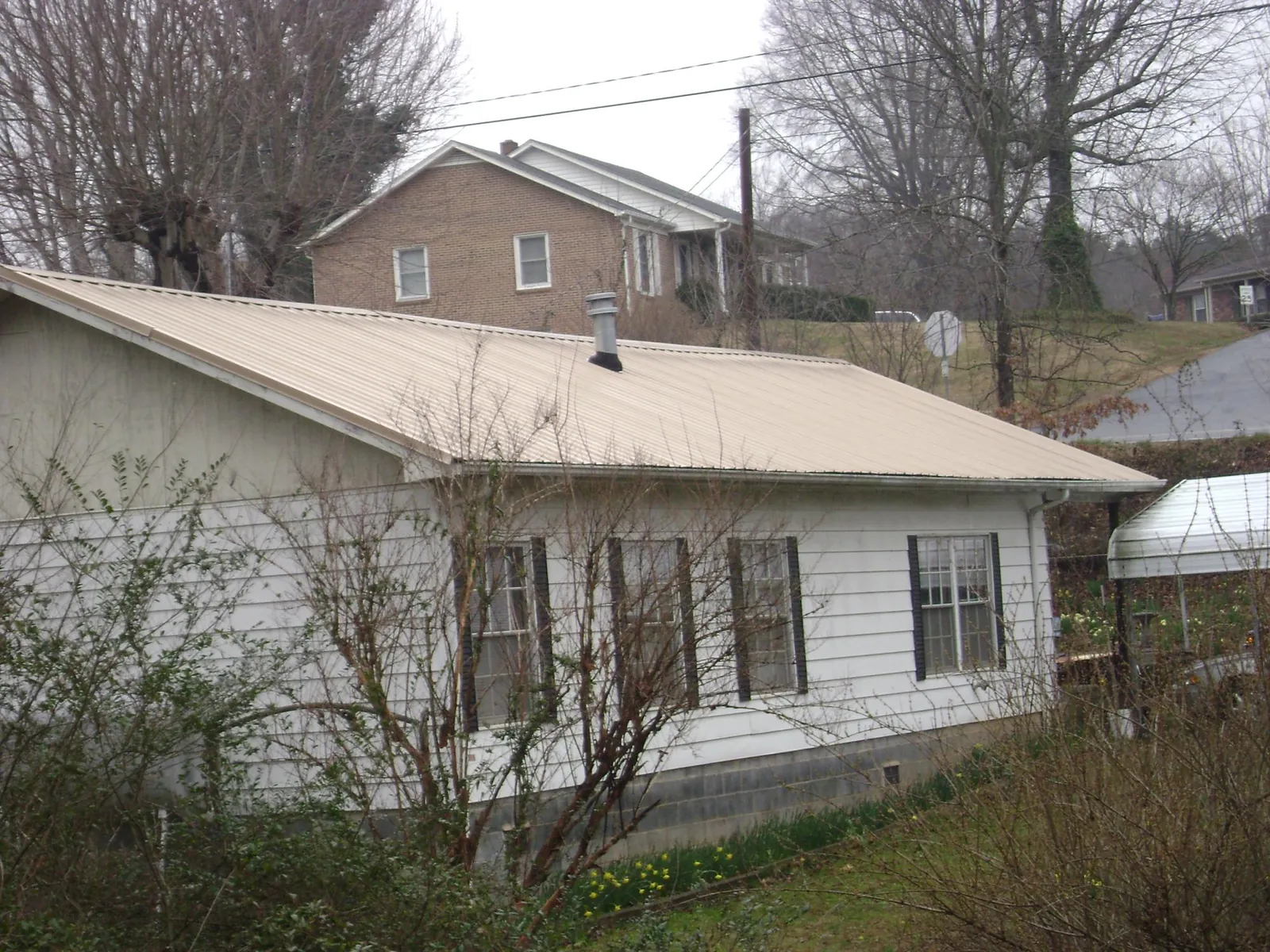 Tan metal roof on a white sided house set into a hillside — Commercial Roofing by Roofing Brothers in Ranchita